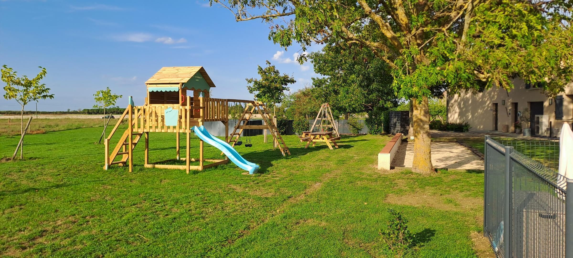 A playground with a slide and swings, surrounded by grass and trees.