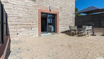Un edificio con fachada de piedra, puerta de acceso de vidrio y un patio con mobiliario exterior.