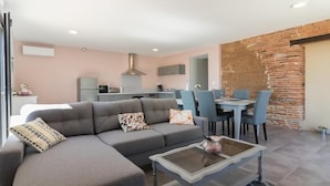 A modern living room with a grey sofa, a glass coffee table, and a dining area with blue chairs. - Domaine le Caprougeat - Chic countryside (Daux)