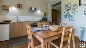 A modern kitchen with wooden cabinets, a built-in oven, and a dining area with a wooden table and chairs. - Gîte du Pradel - Saint-Jory (Saint-Jory)