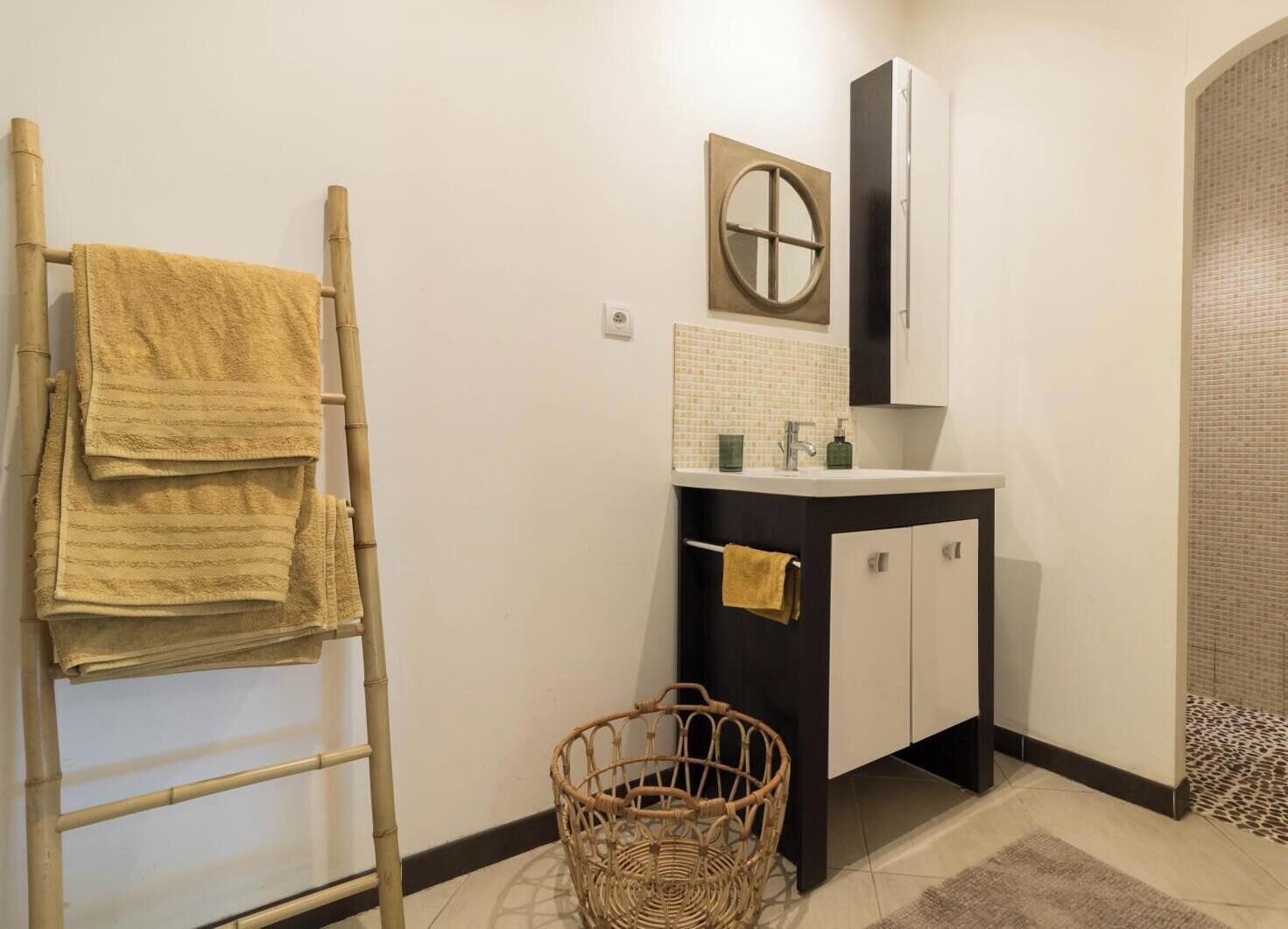 A bathroom with a bamboo towel rack, a wicker basket, and a tiled floor.