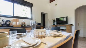 Un coin repas avec une table dressée pour quatre personnes, un téléviseur et une fenêtre donnant sur un paysage verdoyant.