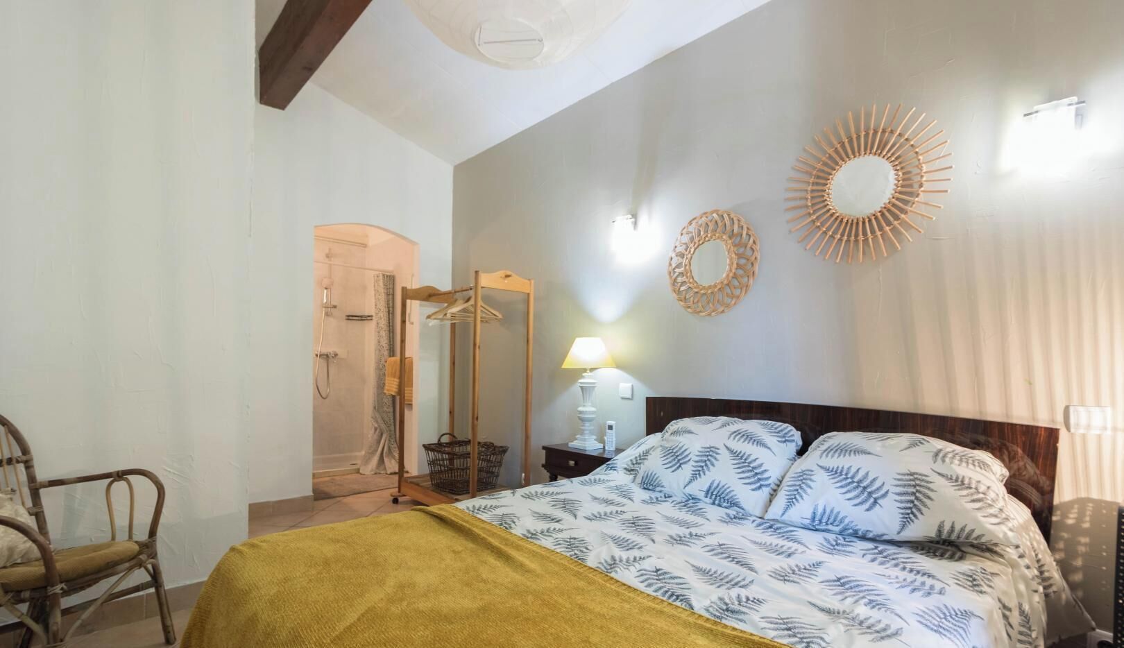 Een slaapkamer met een bed, een houten stoel, een spiegel, een wandlamp en een deur naar een badkamer.