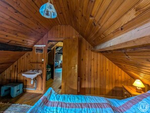 A cozy attic bedroom with wooden walls, a bed, a nightstand, a lamp, and a bathroom with a sink. - Near the church - Garin (Garin)