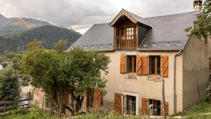 Une maison de campagne au toit à forte pente, avec des volets en bois et des fondations en pierre.
