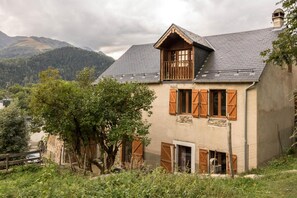 A rustic house with a sloped roof, wooden shutters, and a stone foundation. - Near the church - Garin (Garin)