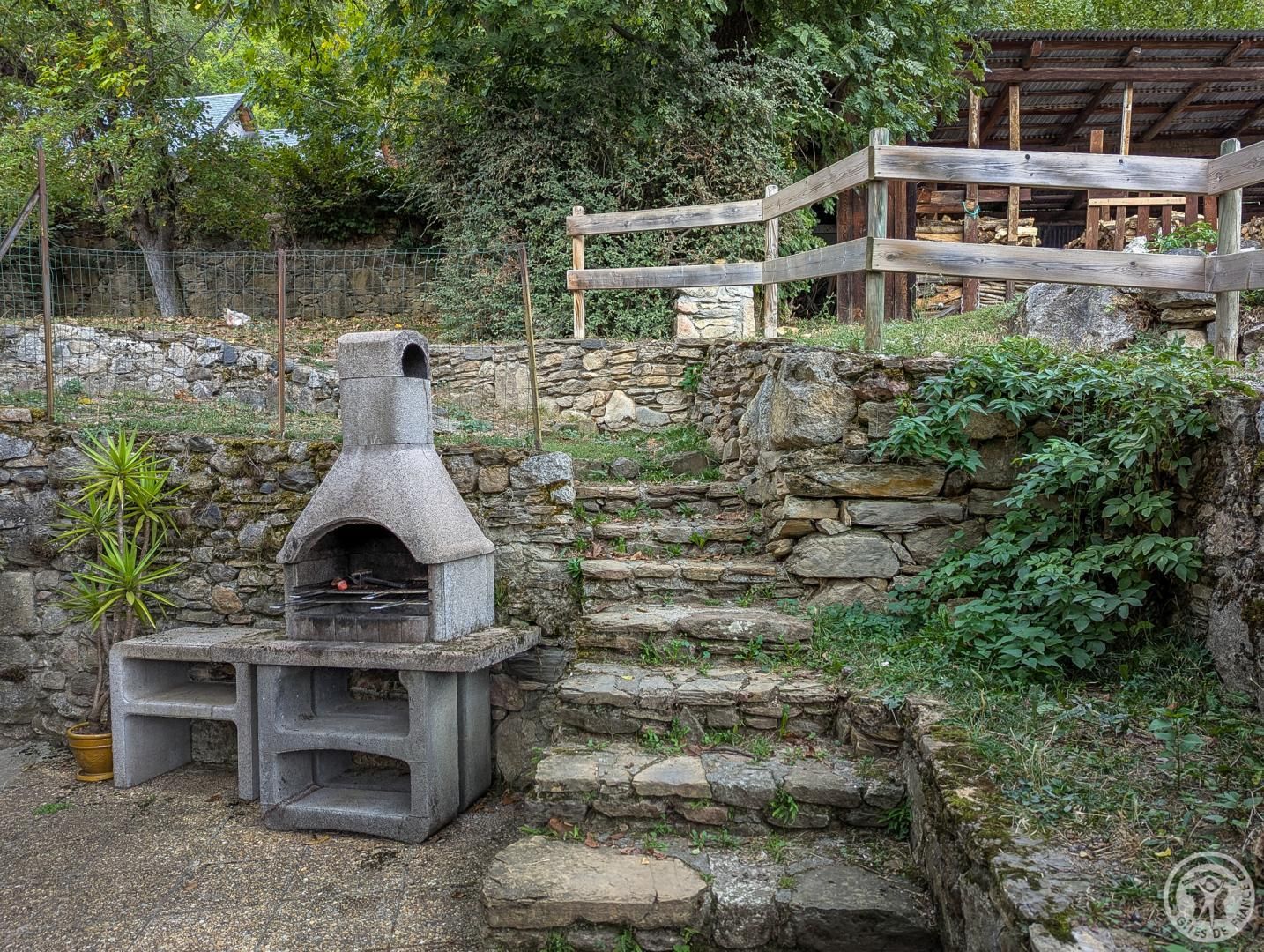A stone-built outdoor oven, a wooden bench, and a stone wall in a garden setting.