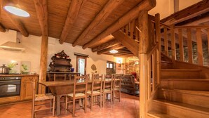 Un intérieur rustique avec un escalier en bois, un coin repas avec des chaises en bois et une cuisine équipée d’une cuisinière et de placards.