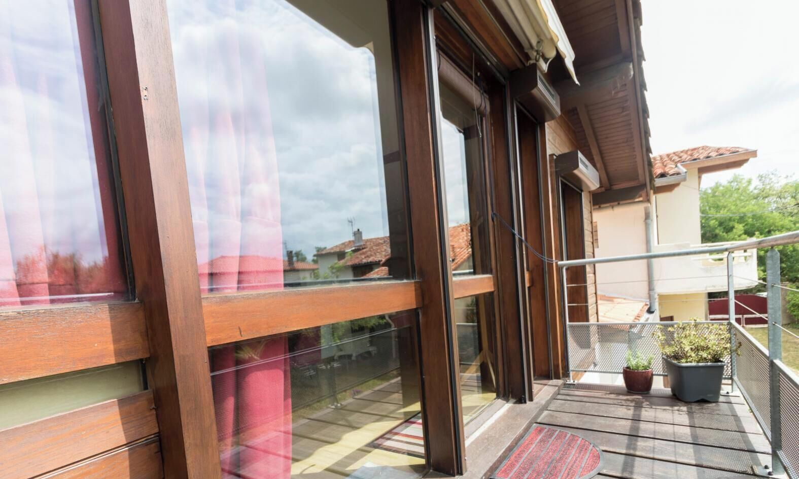 A balcony with a wooden floor, potted plants, and a metal railing.