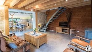 Een ruime woonkamer met houten plafond, een trap, een eethoek en een televisie.