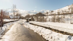 Una carretera rural cubierta de nieve con muros de piedra a ambos lados, que conduce a un portón.