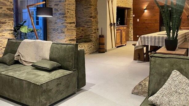 Una sala de estar acogedora con pared de piedra, un sofá verde, un mueble de madera y una zona de comedor con mesa y sillas.
