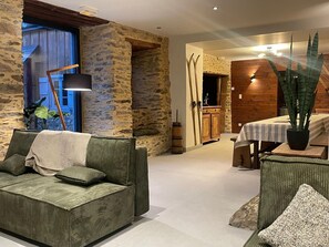 A cozy living room with a stone wall, a green sofa, a wooden cabinet, and a dining area with a table and chairs. - Arza Mendi - Jurvielle (Jurvielle)