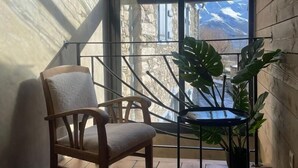 Una habitación con suelo de madera, una silla de madera, una planta en maceta y un ventanal con vistas a montañas.