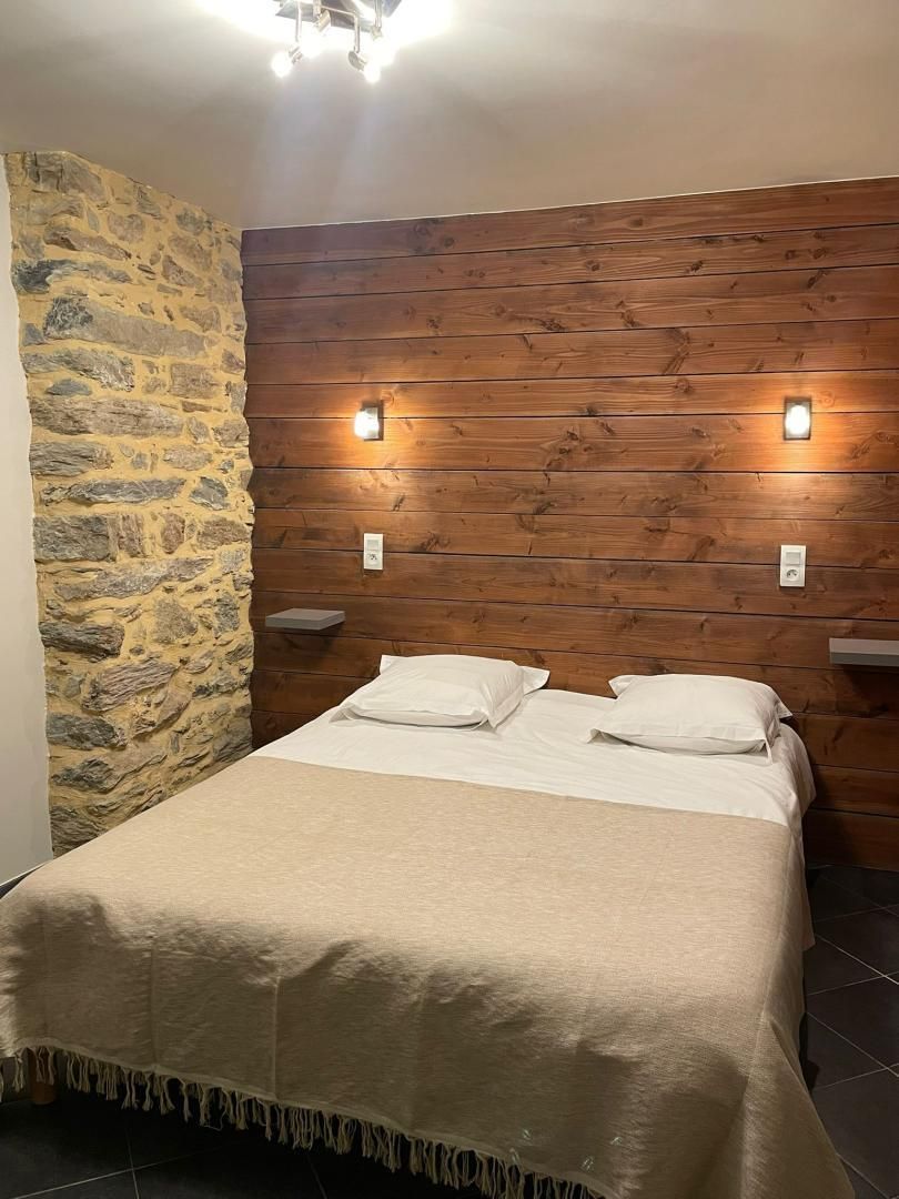 A bedroom with a stone wall, wooden headboard, two bedside tables, and a bed with white bedding.