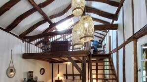 A rustic room with exposed wooden beams, a lofted sleeping area, a bed, a dresser, and a staircase. - Chez Pailhas - Régades (Régades)