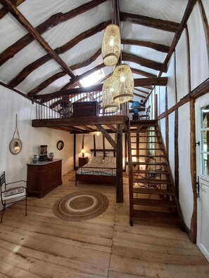 Cozy loft-style bedroom with a large bed, wooden dresser, and staircase leading to an upper level.
