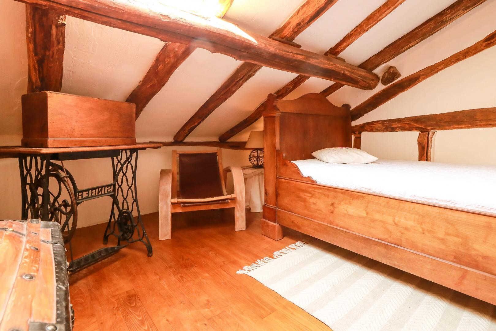 Een gezellige slaapkamer op zolder met een houten bed, een klein tafeltje en een stoel.