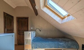 Une petite pièce avec un toit en pente, dotée d’une lucarne, d’un lit, d’un bureau et d’une armoire.