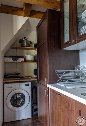 A compact kitchen with wooden cabinets, a built-in washing machine, and a dish rack.