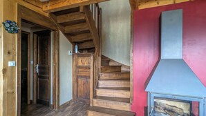 Un escalier en bois mène à une pièce dont un mur est rouge et où se trouve un poêle à bois.