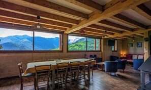A dining area with a table and chairs, large windows with mountain views, and a cozy seating area with a sofa and armchairs.