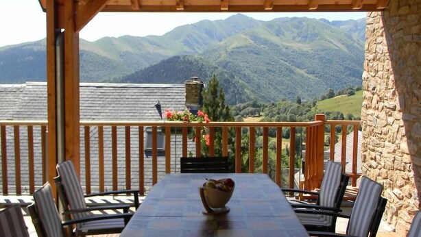 Un espace extérieur abrité, aménagé pour prendre les repas, avec une table et des chaises, offrant une vue sur un paysage montagneux.