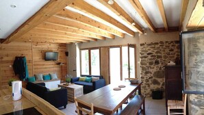 L’intérieur chaleureux d’un chalet avec des murs en bois, un mur en pierre, un canapé, une table à manger et un téléviseur fixé au mur.