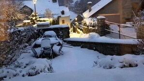 Un espace extérieur enneigé, avec un mur de pierre, un chalet en bois et une chaise en métal.