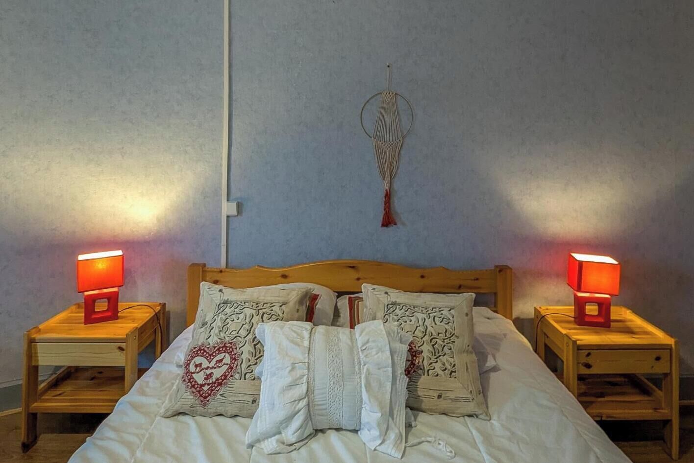 Une chambre à coucher avec un lit en bois, deux tables de chevet avec des lampes, une décoration murale et un coussin en forme de cœur.