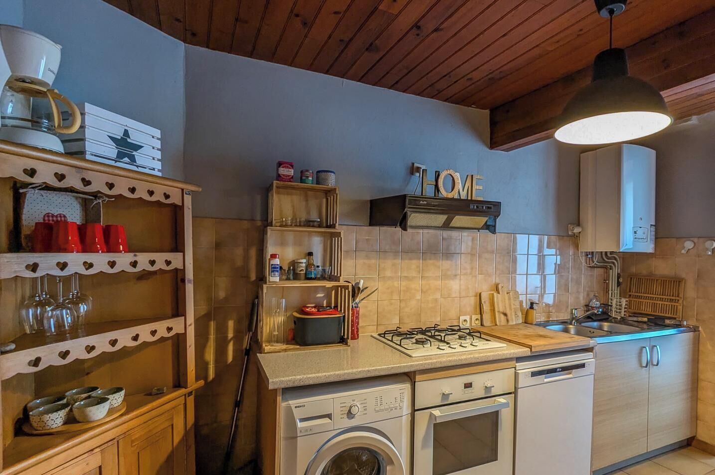 Uma cozinha compacta com fogão a gás, forno, lava-louças e prateleiras de madeira com formatos de coração.
