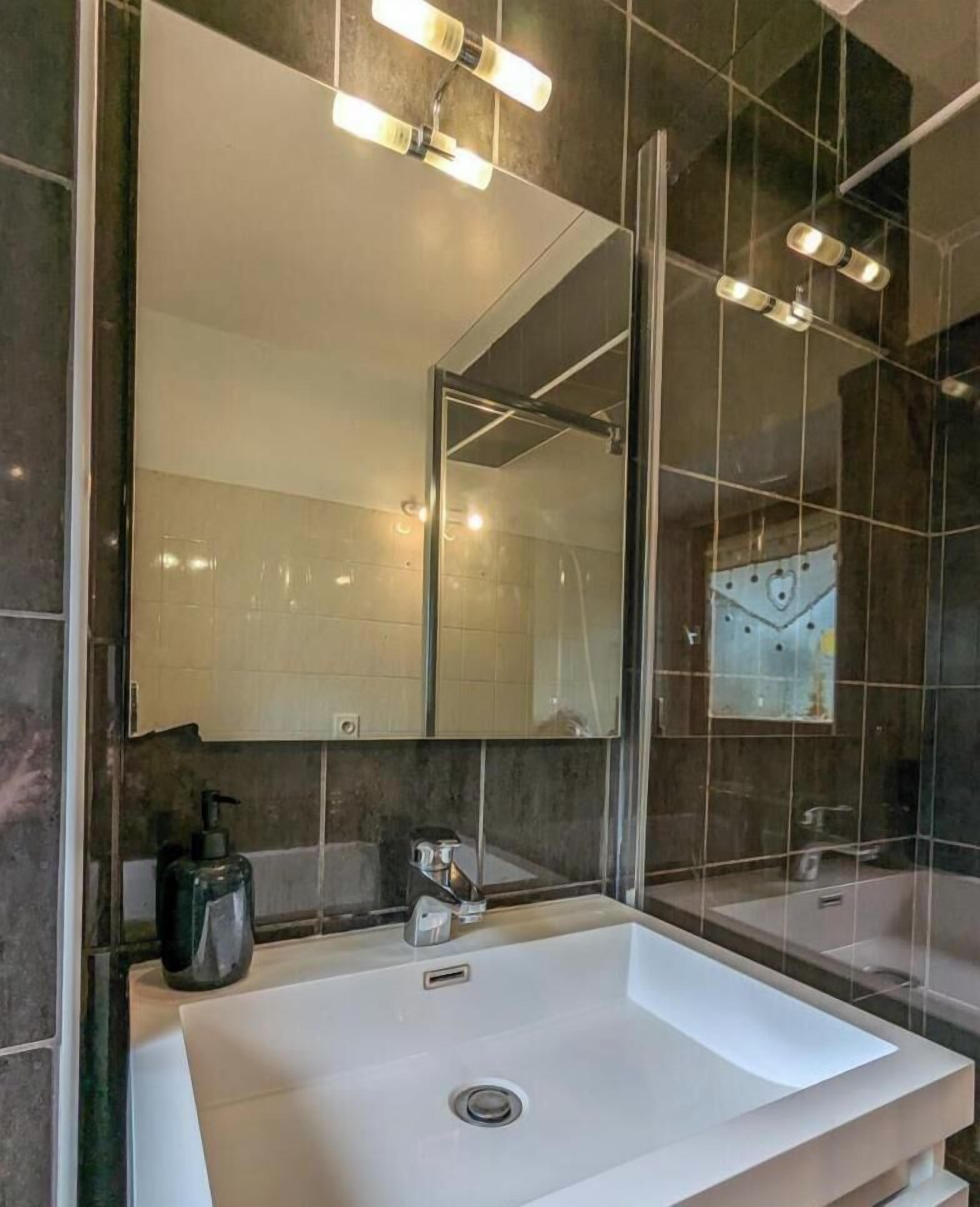 Un baño moderno con un espejo grande, un lavamanos blanco y una zona de ducha.