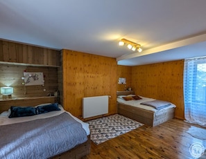 Una habitación con dos camas, paredes de madera, un radiador, una lámpara en el techo y una ventana con cortina.