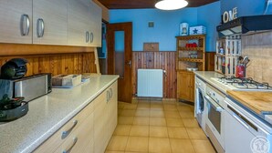 Une cuisine avec des meubles de rangement en bois, un plan de travail, une cuisinière, un évier et un luminaire suspendu.