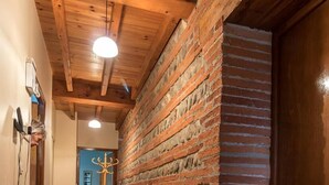 Un couloir avec des poutres apparentes, un mur en briques et une porte en bois.