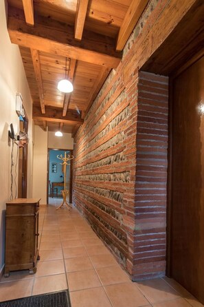 Un pasillo con vigas de madera a la vista, pared de ladrillo y puerta de madera.