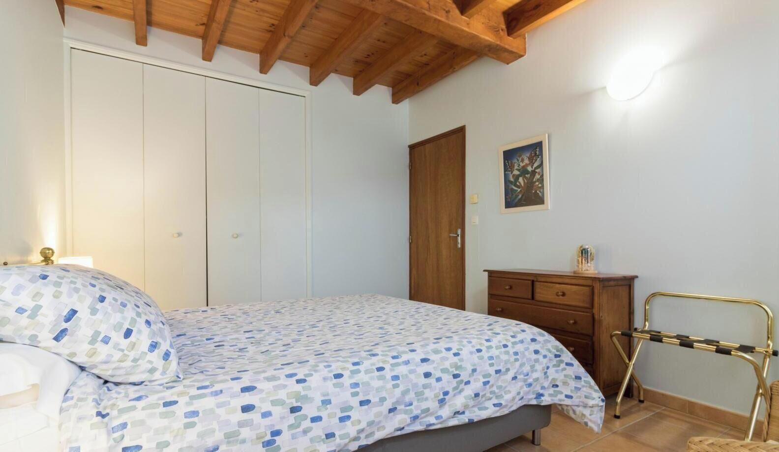 Um quarto com cama, guarda-roupa, penteadeira, uma cadeira e um quadro na parede.