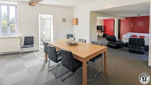 A modern living room with a wooden dining table, black chairs, a red accent wall, and a sofa. - Le Cagire - Labarthe-Rivière (Labarthe-Rivière)