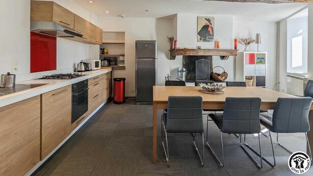 A modern kitchen with wooden cabinets, a stainless steel refrigerator, and a dining area with a wooden table and chairs. - Le Cagire - Labarthe-Rivière (Labarthe-Rivière)