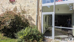 A stone building with a wooden shutter, a glass door, and a small patio area with outdoor furniture. - Le Cagire - Labarthe-Rivière (Labarthe-Rivière)