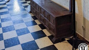 Een kamer met een geruit vloertje, een houten bankje, een kroonluchter en een kapstok aan de muur.