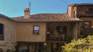 Un bâtiment à deux étages, doté d’un toit en tuiles, d’un balcon avec des chaises et d’un jardin où poussent des cactus et d’autres plantes.