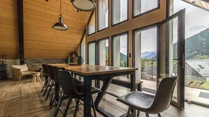 A spacious room with a wooden ceiling, large windows offering a mountain view, a wooden table with chairs, and a stone wall. - La Grange de Mayrègne - MAYREGNE (MAYREGNE)