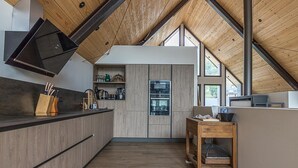 A modern kitchen with wooden cabinetry, a built-in oven, and a dining area with a table and chairs. - La Grange de Mayrègne - MAYREGNE (MAYREGNE)