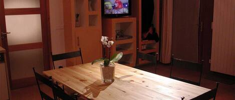 Un tavolo da pranzo in legno con sedie, un televisore su uno scaffale e un vaso con fiori.