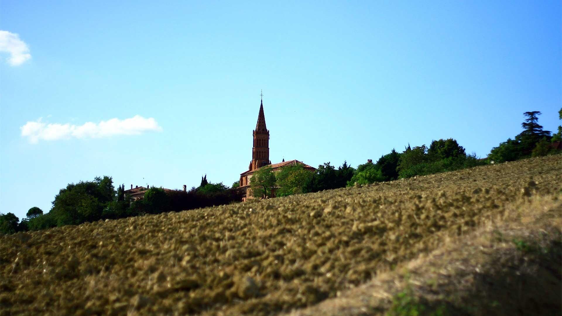 Una iglesia con una aguja alta en una colina, rodeada de árboles y un cielo despejado.
