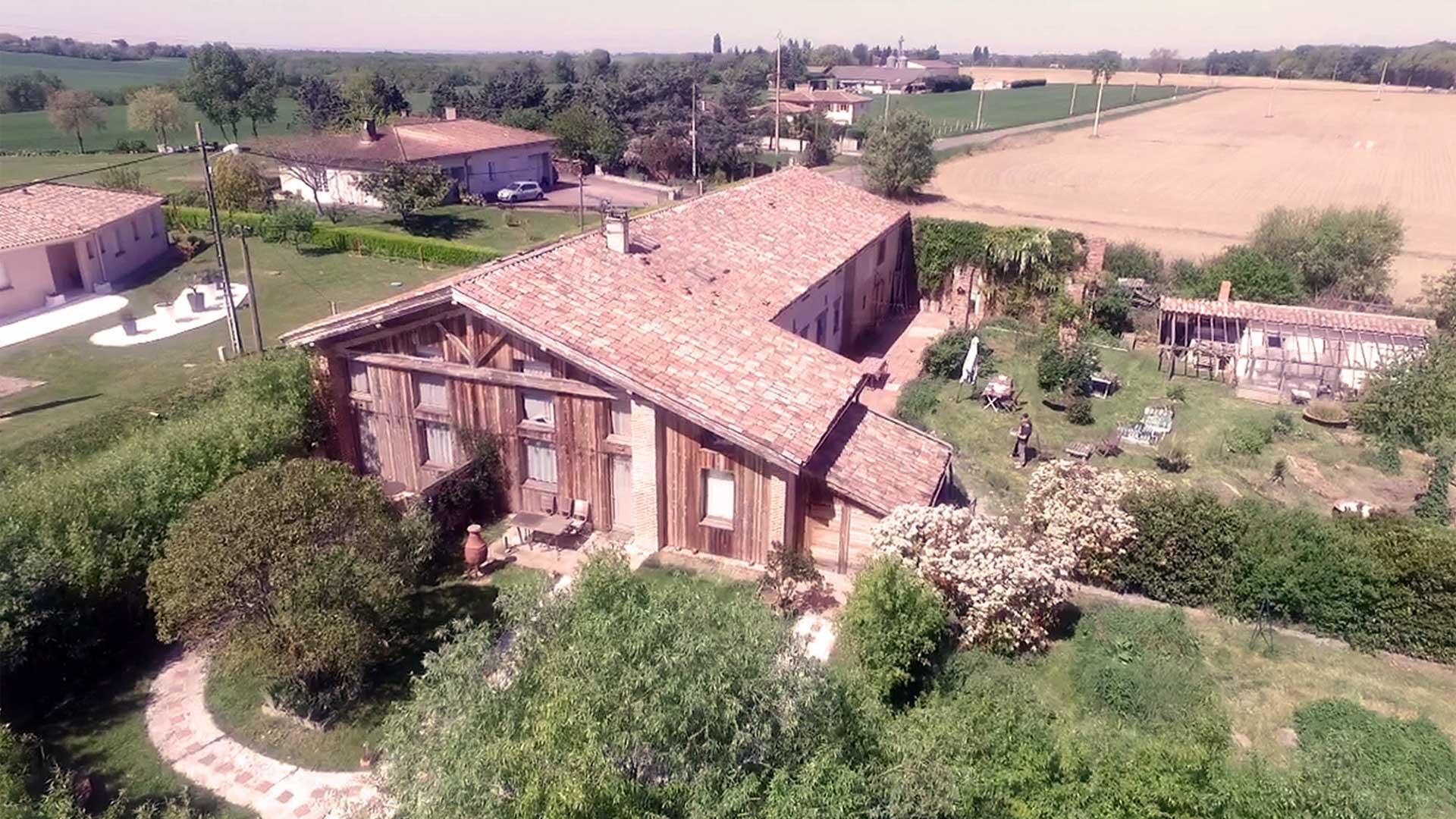 A large, rustic barn with a tiled roof, surrounded by lush greenery and open fields.
