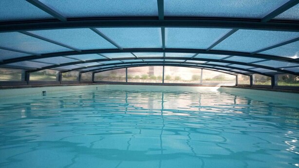 Une piscine intérieure dotée d’un toit en verre et offrant une vue sur l’extérieur.