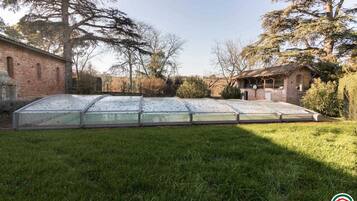 A greenhouse structure with a glass roof and walls, surrounded by a grassy area and trees.
