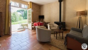 Un salon avec une cheminée, un téléviseur et un coin repas agrémenté d’une nappe rouge.